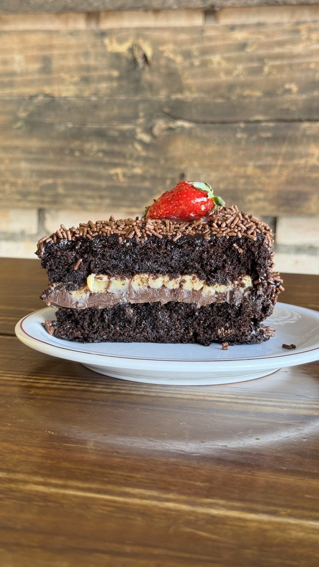 Fatia de bolo de chocolate recheado, coberto com granulado e morango